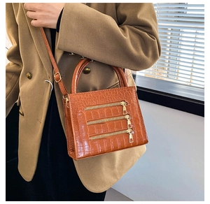 Brown crocodile embossed handbag with golden zippers worn by a model in a camel blazer