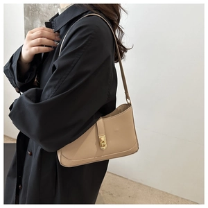 Close-up of beige baguette bag with leather strap and golden turn-lock metal buckle
