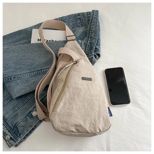 Detail of light beige crossbody bag showing nylon texture, zippers and adjustable strap