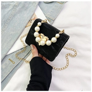 Detail of black mini crossbody bag featuring pearl handle and golden floral clasp