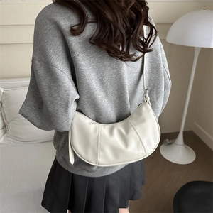 Minimalist white crescent shoulder bag in soft leather shown on model in a modern home setting