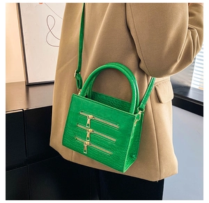 Detailed view of green crocodile pattern handbag with golden zipper accents and top handle