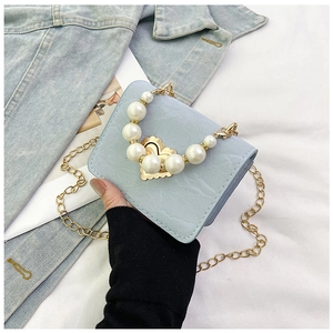 Detail of light blue mini bag with golden heart clasp, pearl handle and chain strap