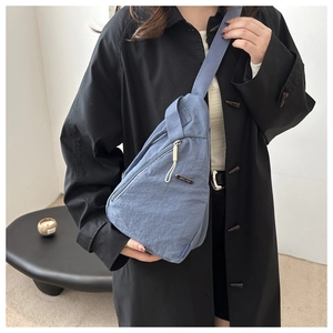 Close-up of blue nylon chest bag featuring pleated texture and diagonal front zipper pocket