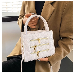 Detailed view of white crocodile embossed handbag with decorative gold zippers and top handle