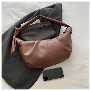 Detail of dark brown leather crescent bag with lychee texture and knotted strap