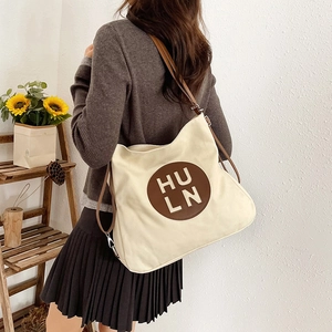 Minimalist beige canvas tote bag with brown leather straps and embossed letter patch