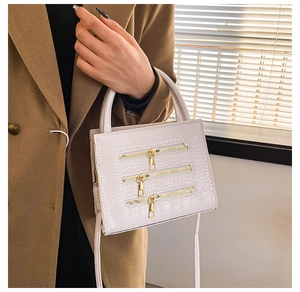 Close-up of white crossbody bag with crocodile texture and triple gold zipper detail