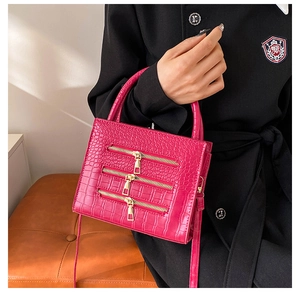 Close-up of fuchsia crocodile texture handbag featuring three decorative gold zippers