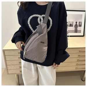 Detail of grey nylon crossbody bag showing water-resistant texture and metal logo plate