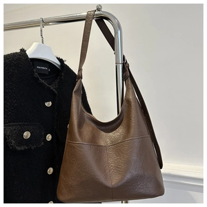 Détail d'un grand sac hobo vintage marron avec surpiqûres accroché sur un cintre en métal