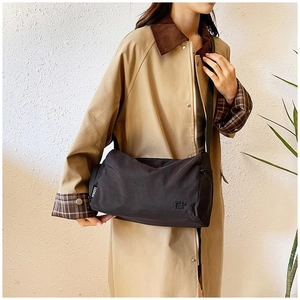 Detail of black nylon shoulder bag with fashion label on a person wearing a trench coat