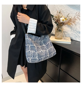 Detail view of the wide black strap and blue geometric canvas tote worn with a black coat