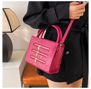 Detail of rose red crocodile pattern handbag with decorative golden zippers on premium leather