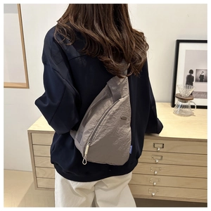 Detail of grey crossbody sling bag with crinkled nylon texture and side fashion label