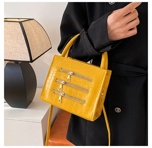 Detail of crocodile embossed yellow leather handbag with decorative zippers and handle