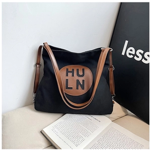 Detail of a black canvas hobo bag with brown leather straps and round logo patch