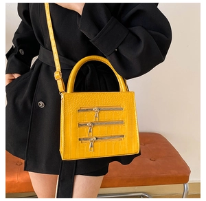 Detail of yellow crocodile pattern handbag with three decorative zippers on the front