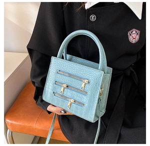 Detail of light blue crocodile embossed tote bag with triple zippers and gold hardware