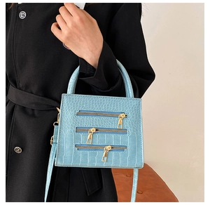 Close-up of light blue crocodile texture handbag with decorative gold metal zippers