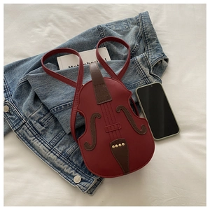 Detail view of red violin-shaped crossbody bag on denim jacket with lifestyle props