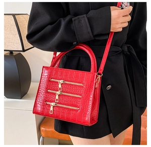 Macro detail of red crocodile texture handbag with decorative gold zippers and top handle