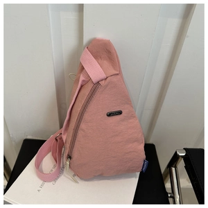 Detail of pink nylon crossbody chest bag with metal brand logo on a white book surface
