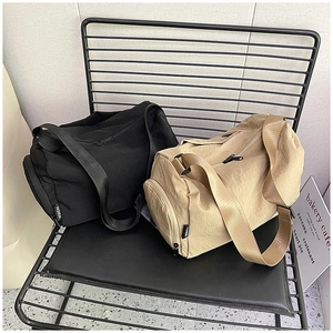 Detail view of black and khaki cylindrical nylon shoulder bags on a metal chair