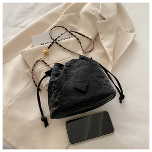 Macro shot of black pleated bucket bag with gold chain strap and smartphone for size scale