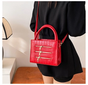 Detail of red crocodile texture handbag featuring decorative triple golden zippers