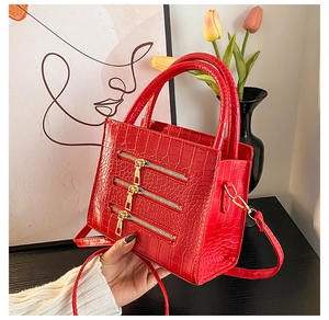 Detail of red crocodile texture handbag with decorative gold zippers and dual handles