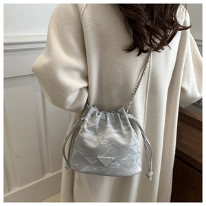 Detail of grey drawstring bucket bag with marble texture and elegant chain strap worn by model
