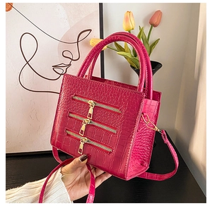 Detail of rose red crocodile embossed handbag featuring three decorative gold zippers