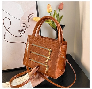 Detail of brown crocodile pattern handbag with triple zipper design and long strap