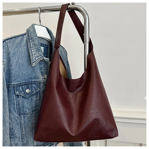 Detail of burgundy leather tote bag texture and wide shoulder strap on a hanger