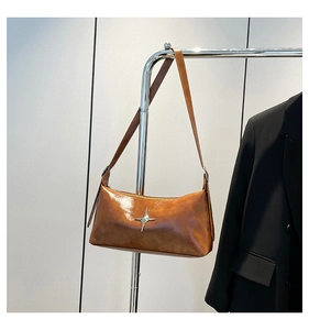 Detail of a brown glossy leather shoulder bag featuring a silver metal cross star charm
