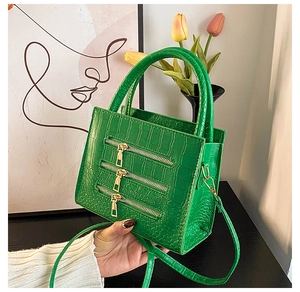 Detail of green crocodile textured handbag featuring three golden decorative zippers