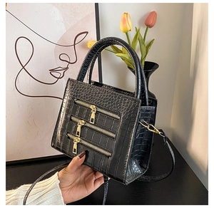 Detail of black crocodile texture handbag with triple gold zipper accents and dual handles