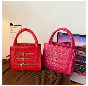 Detail of red and fuchsia croc-embossed handbags with triple zipper gold hardware