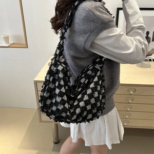Fashionable denim canvas checkered hobo bag with tassel fringe detail shown on shoulder