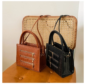 Close-up of crocodile embossed leather texture with triple zipper accents on handbags