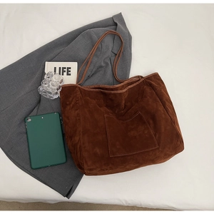 Detail of a brown suede tote bag with a front patch pocket on a cozy bedroom background