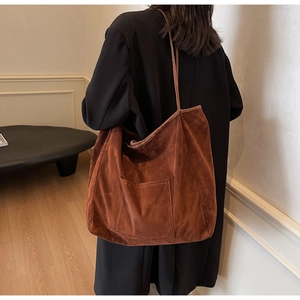 Detail view of large dark brown suede tote bag with front pocket shown on shoulder