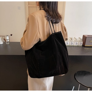 Detail of minimalist black suede tote bag with front pocket in cozy cafe setting