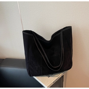 Detail shot of a large black suede tote bag with a minimalist front pocket and soft texture