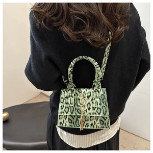 Detail of green leopard print crossbody bag with gold logo and tassel on a model