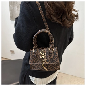 Detail of leopard print crossbody bag with gold metal logo and tassel on model