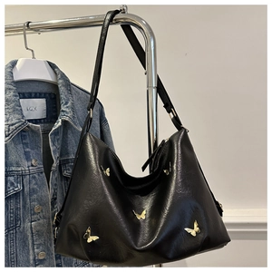 Detailed close-up of golden butterfly metal accents on black pebbled leather tote bag