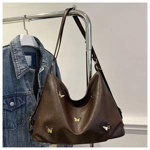 Detail of dark brown faux leather shoulder bag with decorative golden butterfly rivets