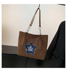 Detail of suede tote bag with blue denim star patch and metal chain strap accent